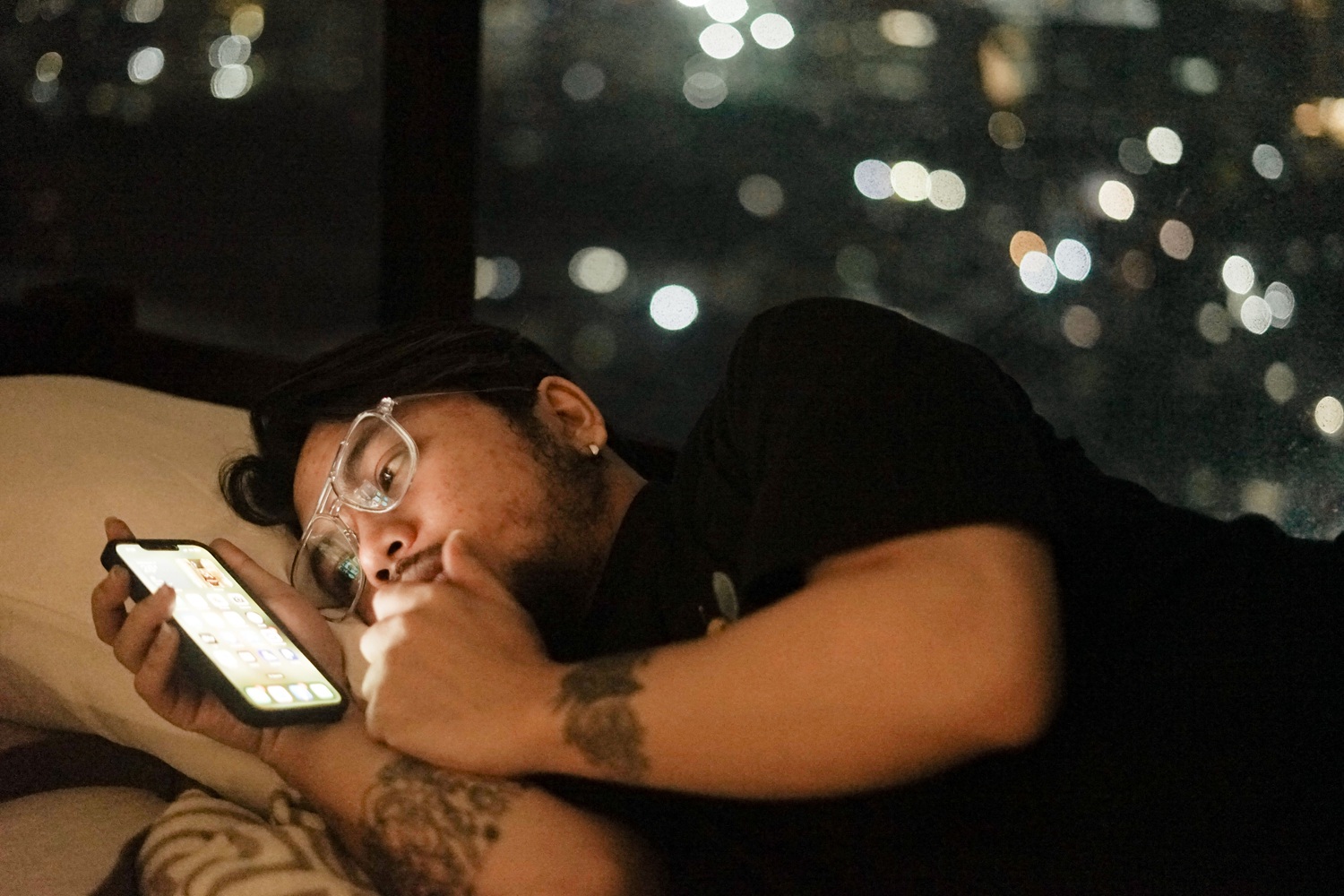 A man lying in bed at night, illuminated by his phone screen.