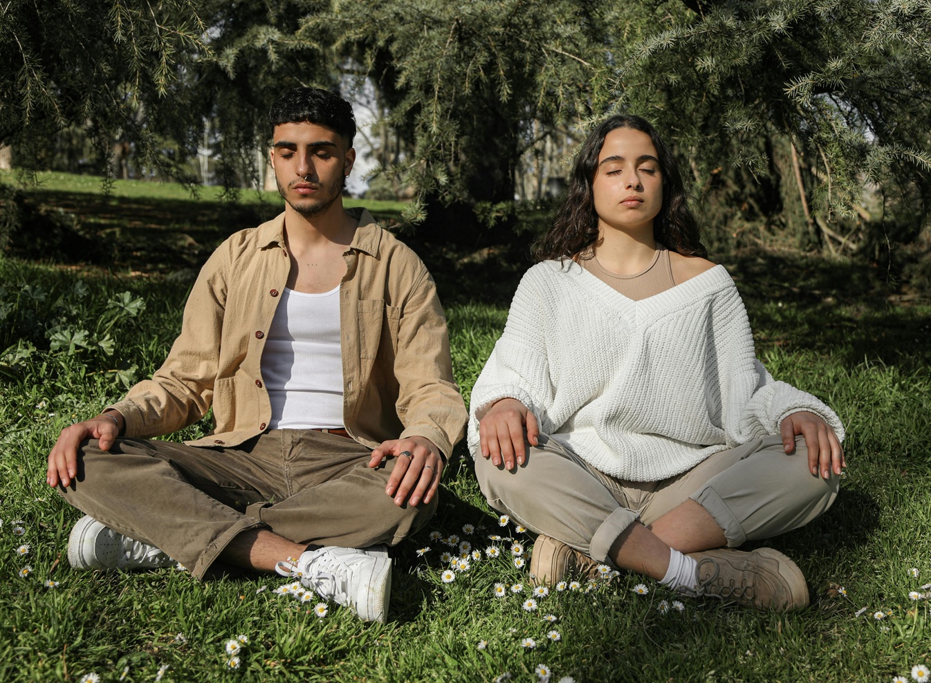 Two individuals meditating in a serene park setting. Peaceful and relaxed environment.
